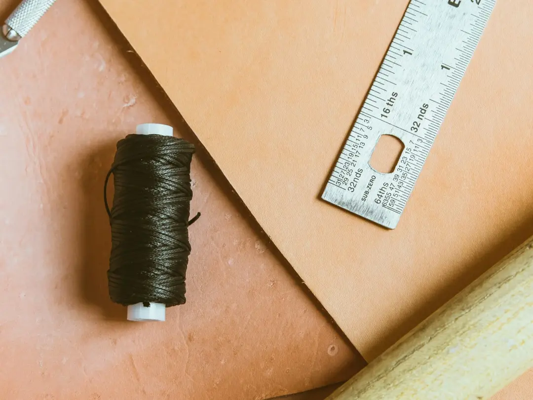 Leather hide, a steel ruler and a reel of thread on a workbench